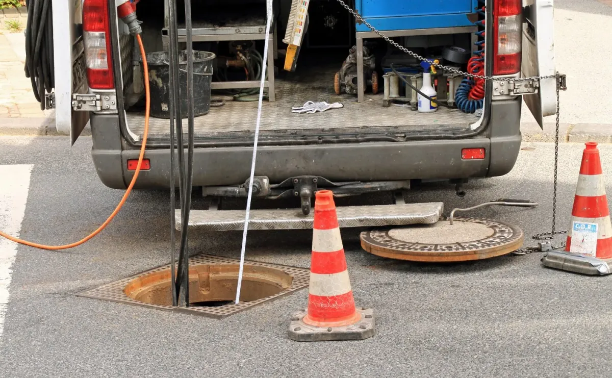 Drainage engineers van and equipment at an open manhole on a road, performing outdoor drain unblocking or repair.