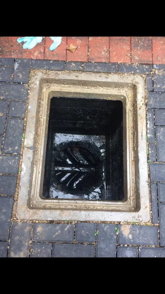 An overhead view of an open outdoor drain inspection chamber full of standing water, suggesting a blockage or overflow.