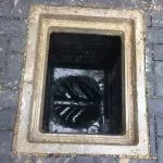 Open external drain gully showing dirty water and debris inside, suggesting a blockage or need for cleaning.